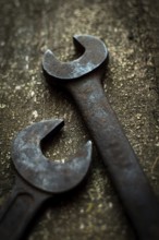 Two aged metal wrenches lie on a rugged wooden surface, illustrating their wear and the importance
