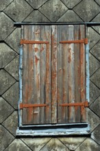 Closed wooden shutters with peeling paint rest against an aged building, highlighting the rustic