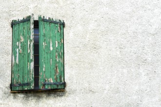 Weathered green shutters stand slightly ajar on a textured white wall, showcasing the charm of an