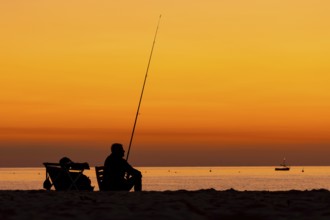 A man fishing just in front of sunrise on the Costa Rei, a coastline of the Italian island of