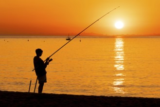 A boy fishing shortly after sunrise on the Costa Rei, a coastline of the Italian island of