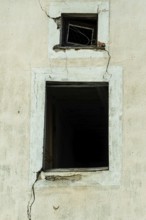 Cracked walls and dark empty windows show the neglect of an abandoned structure. The peeling paint