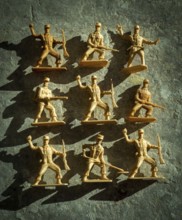 Plastic toy soldiers are displayed in different action poses on a textured surface, casting shadows