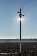A power pole stands tall in the foreground, with sunlight shining directly behind it, creating a