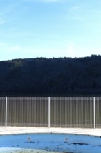 A swimming pool reflects the blue sky and surrounding mountains. A metal fence surrounds the space,