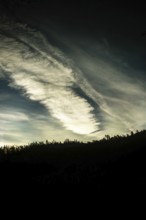 Cloud patterns swirl dramatically in the twilight sky, contrasting against the dark outline of a