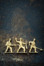 Three vintage toy soldiers in different poses rest on a rugged, textured surface. Their playful