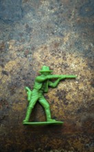 A small green plastic toy cowboy stands firmly on a rustic blue and brown textured background. The