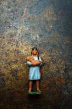 A vibrant plastic figure represents an Indian Native American woman cradling a child, positioned on