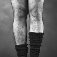 Close-up view of a pair of hairy male legs positioned together, wearing thick black mid-calf socks,