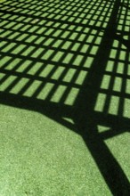 A grid of shadows falls across vibrant green turf, formed by a lattice overhead. The sunlight