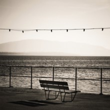 A solitary bench sits by the lakeside promenade in Nyon, Switzerland. Gentle waves ripple in Geneva
