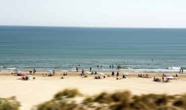 Sunbathers and swimmers relax on the sandy beach by the tranquil Mediterranean Sea. The atmosphere