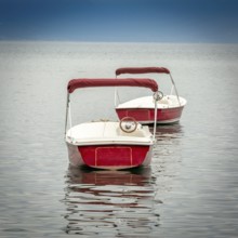 Several small red boats rest on the peaceful surface of Lake Geneva, reflecting the clear blue sky.