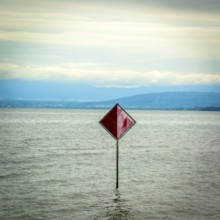 A prominent red information sign rises above the water of Lake Geneva, indicating safety or