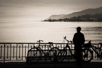 A tourist stands at the edge of Lake Geneva, captivated by the serene waters and distant hills.