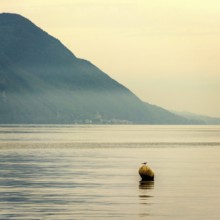 A buoy bobs gently on the calm waters of Lake Geneva, surrounded by serene mountains. The early
