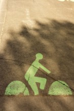 A green bicycle lane marking is visible on a city street, featuring a cyclist silhouette. Shadows