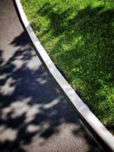 A smooth, dark asphalt path curves alongside vibrant green grass, creating a tranquil atmosphere.
