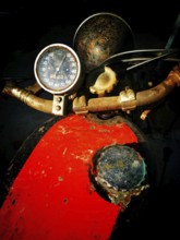 A worn motorcycle dashboard features a rusty speedometer and a faded paint job. The dark background