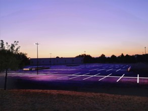 A quiet parking lot in France at dusk, illuminated by streetlights. The clear sky transitions from