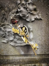 A dried rose with delicate yellow petals lies against a textured, weathered gravestone featuring