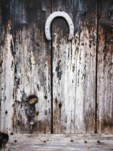 A rustic wooden door features a weathered texture, complete with a vintage horseshoe mounted at the