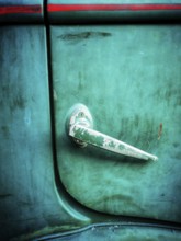 A close-up view of a vintage car door handle featuring a weathered surface and vibrant green paint.