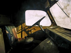 An abandoned truck interior features worn seats and an aged steering wheel, casting shadows against