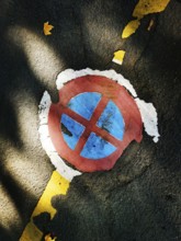 A circular parking symbol with red and blue colors appears worn and cracked on an asphalt surface.