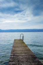 A sturdy jetty extends into the serene waters of Lake Geneva, surrounded by mesmerizing blue hues