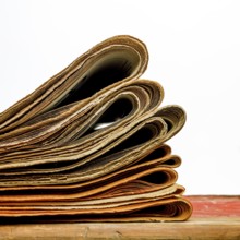 A stack of newspapers lies neatly on a white background, displaying an assortment of folded pages