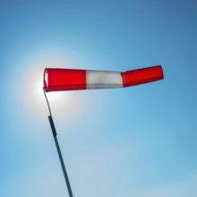 A vibrant windsock attached to a pole is fluttering in the wind against a clear blue sky. The