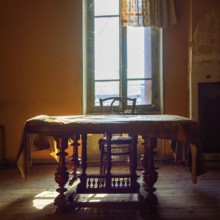 Warm sunlight filters through an old window, illuminating a vintage wooden table and chair. Dust