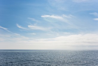Dark ocean under a clear blue sky with bright white feathery clouds, cloud bank, horizon, water