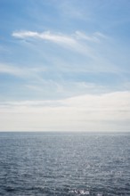 Dark ocean under a clear blue sky with bright white feathery clouds, cloud bank, horizon, water