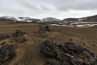 Barren volcanic landscape with snow fields, volcanic rock, mountain peaks with rain clouds,