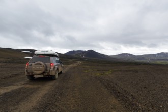 Off-road vehicle, SUV with roof tent driving on gravel track, barren volcanic landscape with snow
