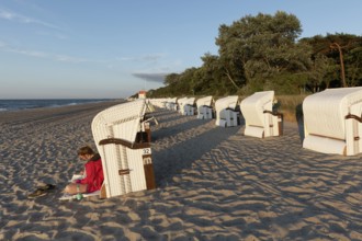 Woman reading a book in the evening sun, leaning against a beach chair, Baltic Sea near