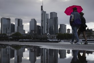 Two people walking in the rain under an umbrella in front of the Frankfurt bank skyline along the