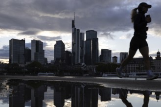 A jogger runs in the rain along the banks of the Main in front of the Frankfurt banking skyline,