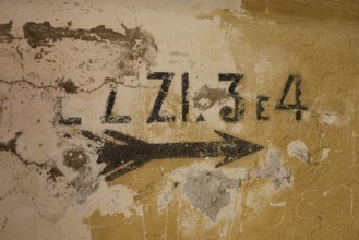 Lost Place, Ruin of a barracks, Patched wall with arrows and numbers in black on yellow, weathered