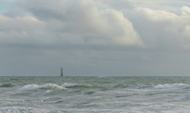Waves crash against the shore while a lone lighthouse looms in the distance under a sky filled with