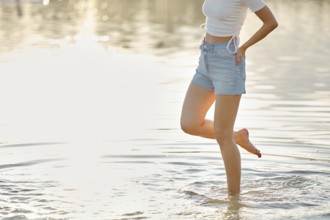 Unrecognizable woman steps carefully in the clear water, enjoying the warmth of the sun on her skin
