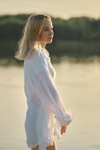 Woman with light blonde hair gazes thoughtfully into the distance while standing near tranquil