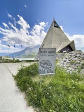 In front sign for Jardin Alpin, behind it pyramid museum with stylised pyramid in memory of the