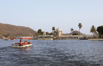 Excursion boat on Lake Pichola, behind Jagmandir Island Palace or Lake Garden Palace, Udaipur,
