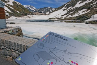 Tourist information board of Great St. Bernard Pass, behind it pass summit with icy lake Lago di