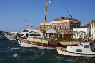 Wooden boats in the harbour with bright facades and Greek flags in calm waters, Agia Marina, Leros,