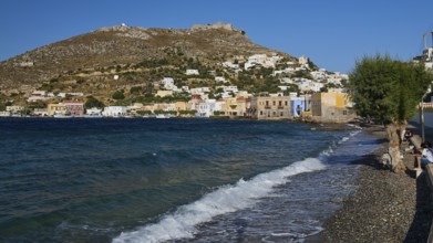 Panteli fortress, beach with pebbles, wavy sea, coast with colourful buildings and hills in the